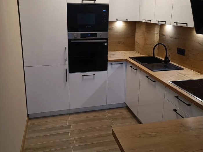 Weiße Küche mit Gerätehochschrank, Holzarbeitsplatte und schwarzer Spüle