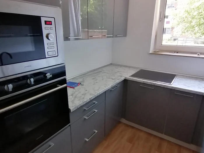 Graue Küche mit heller Steinoptik-Arbeitsplatte, Fenster und Gerätehochschrank