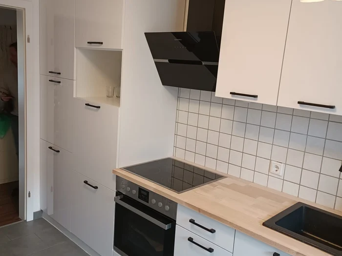 Kleine weiße Küche mit Holzarbeitsplatte, weißen Fliesen und Hochschrank