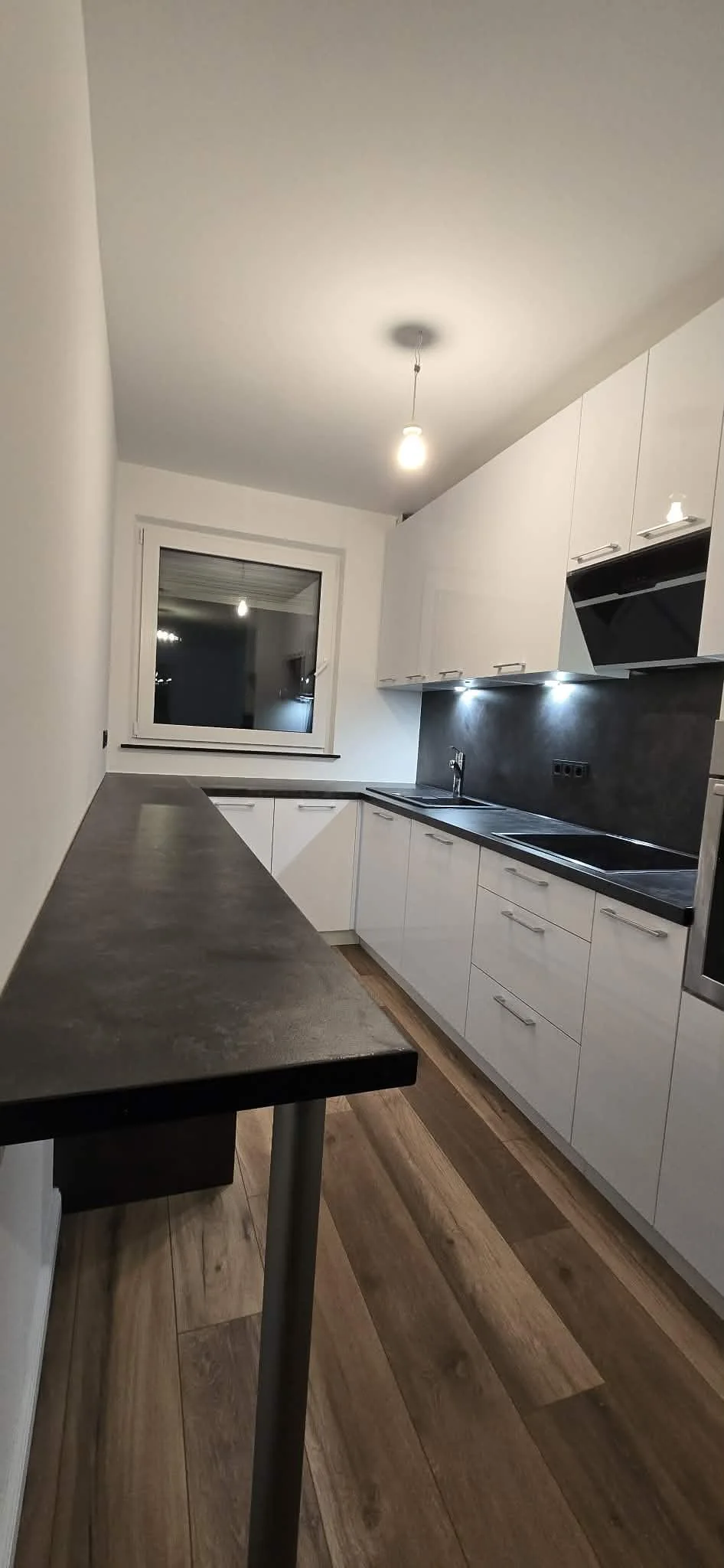 Weiße Küche mit langer dunkler Arbeitsplatte, schwarzer Spüle und Fenster