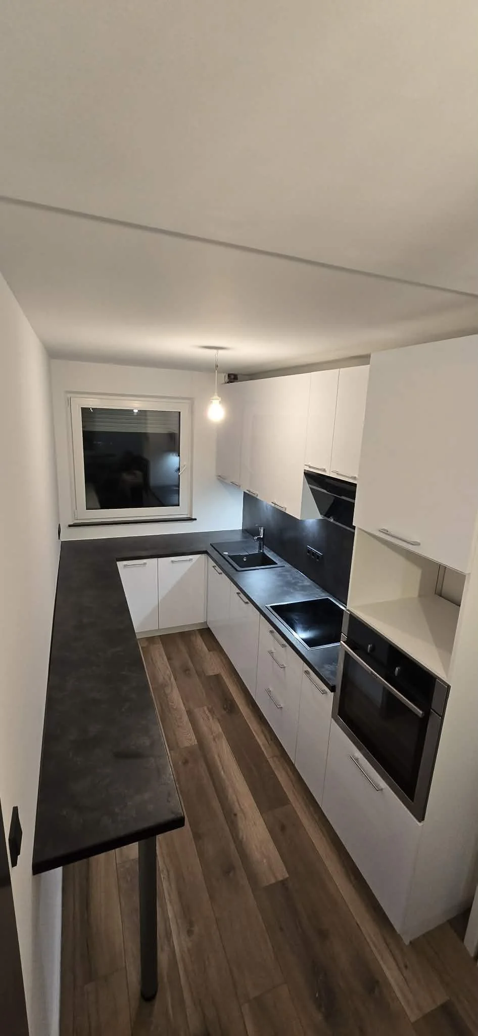 Weiße Küche mit dunkler Arbeitsplatte, schwarzer Spüle und Fenster über der Arbeitsplatte