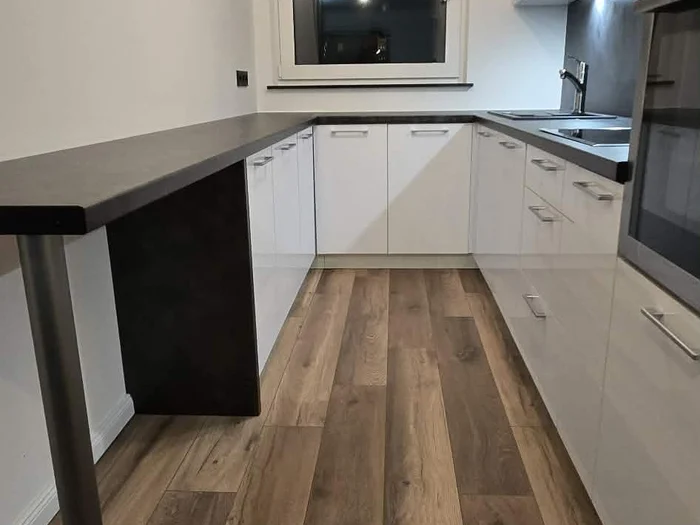 Weiße Küche mit dunkler Theke, Holzfußboden und eingebautem Backofen
