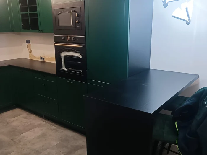 Dunkelgrüne Küche mit schwarzer Arbeitsplatte und Hochschrank mit Backofen